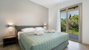 Une chambre à coucher avec un lit, des tables de chevet, une vue sur l’extérieur grâce à une porte coulissante et un balcon.