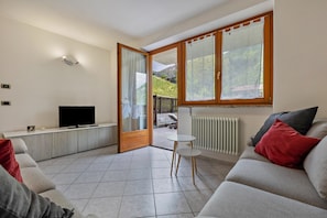 Een woonkamer met een bank, een televisie, een kleine tafel en een schuifdeur naar een buitenruimte.