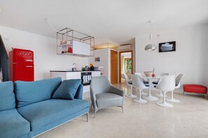A modern living room with a sofa, dining table, chairs, and a kitchen area.