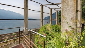 Estrutura de pedra com guarda-corrimão de metal, com vista para a água e montanhas.