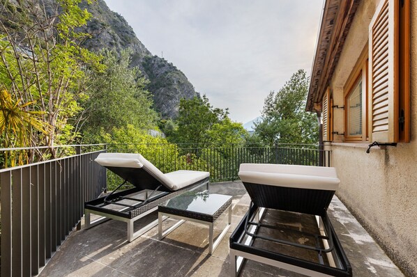 A balcony with two lounge chairs and a small table, overlooking a mountainous landscape.