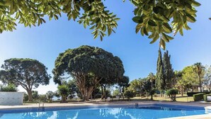 A swimming pool with a tiled deck, surrounded by various trees and a clear sky. - Casa Emilio Apartment with Wi-Fi and Air Conditioning (Benalmádena)