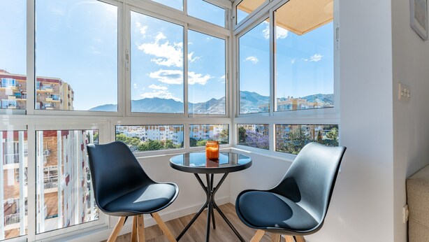 A balcony with two chairs, a glass table, and a view of buildings and mountains. - Casa Emilio Apartment with Wi-Fi and Air Conditioning (Benalmádena)
