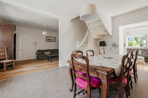 A dining area with a wooden table and chairs, a staircase, and a living room in the background.