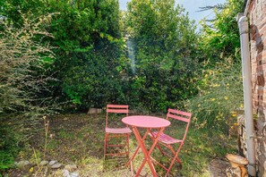 A garden with a red table and chairs, surrounded by dense foliage and a stone wall. - Holiday Home 'Maison Pleneuf Val André Proche Mer' with Private Terrace, Private Garden and Wi-Fi (Pléneuf-Val-André)