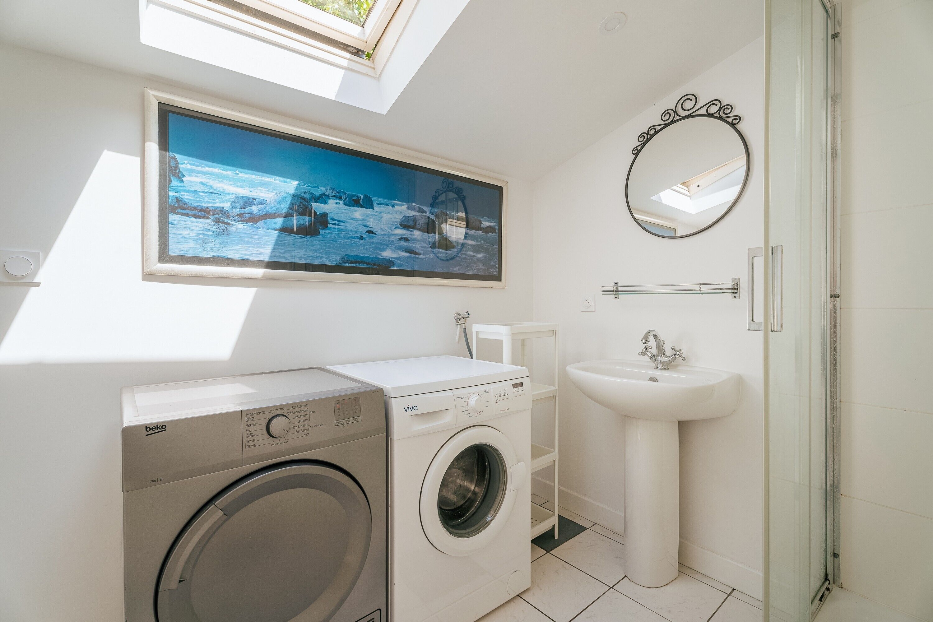 A modern bathroom with a washing machine, a sink, a mirror, and a large window with a view of the ocean.