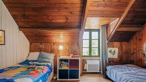 A cabin-style room with wooden walls and ceiling, a bunk bed, a small white nightstand with a lamp, and a window with a view of trees. - Holiday Home 'Maison Pleneuf Val André Proche Mer' with Private Terrace, Private Garden and Wi-Fi (Pléneuf-Val-André)