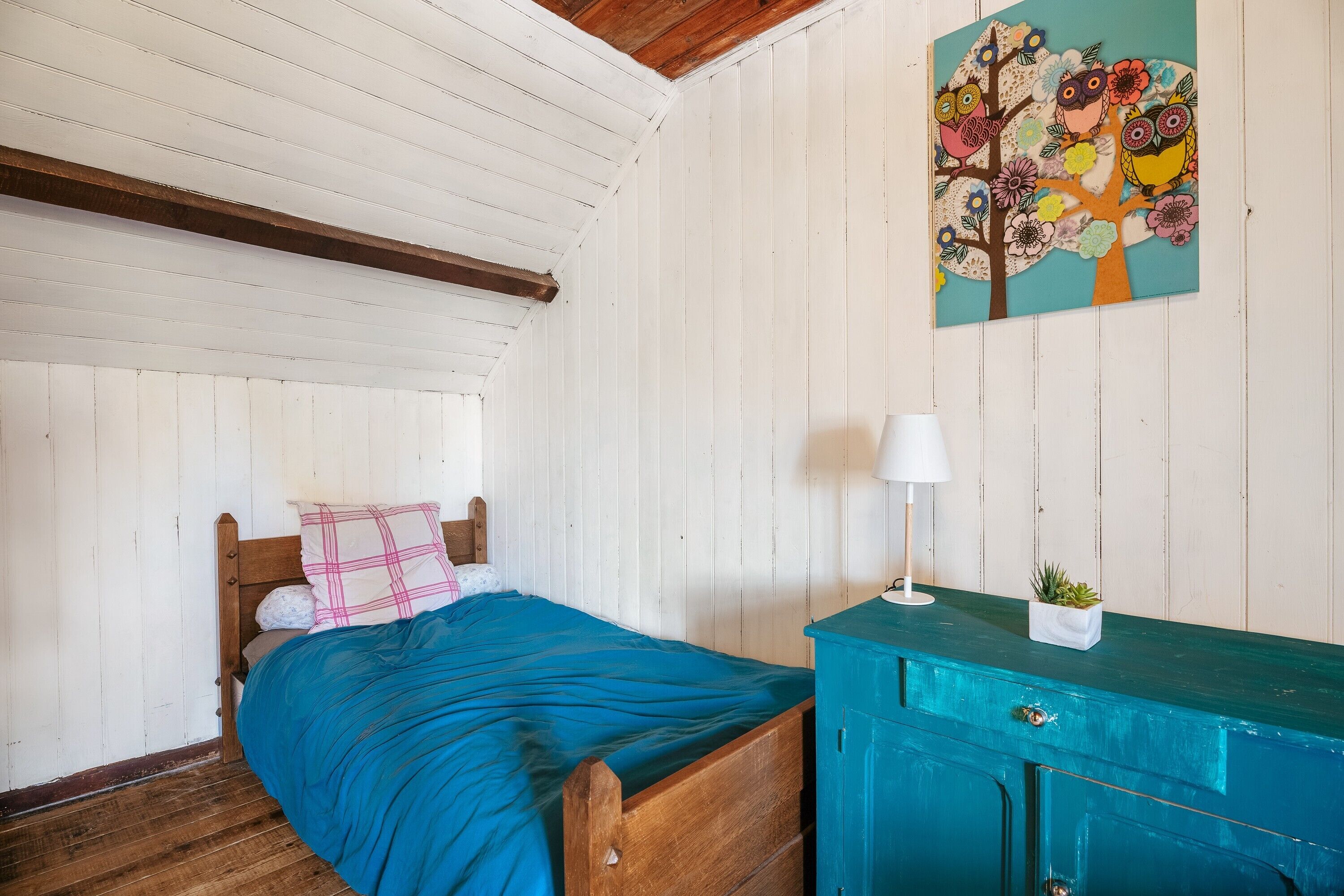 Quarto com cama de madeira, cómoda azul-turquesa e um quadro na parede com corujas e flores.