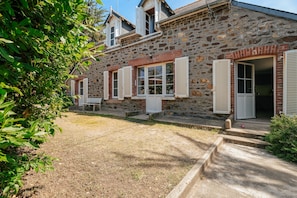 A stone building with a rustic appearance, featuring multiple windows with shutters, a small porch, and a well-maintained lawn.