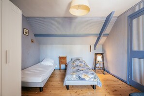 A room with two single beds, a wooden floor, striped wallpaper, a ceiling lamp, and a small table with a lamp. - Holiday Home 'Maison Pleneuf Val André Proche Mer' with Private Terrace, Private Garden and Wi-Fi (Pléneuf-Val-André)