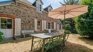 A stone building with a wooden table and chairs, a bench, and an umbrella. - Holiday Home 'Maison Pleneuf Val André Proche Mer' with Private Terrace, Private Garden and Wi-Fi (Pléneuf-Val-André)