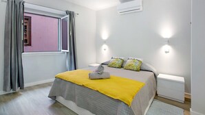 Una camera da letto con un letto, una finestra con tende, un condizionatore e lampade sui comodini.