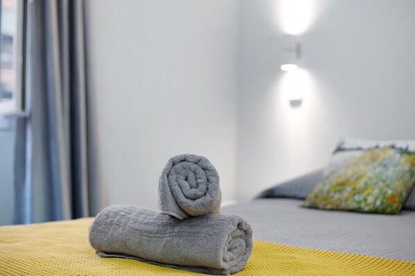 A neatly made bed with a rolled gray towel and a pillow with a floral pattern. - Apartment 'Família Dória Nóbrega T0' with Wi-Fi and Air Conditioning (Funchal)