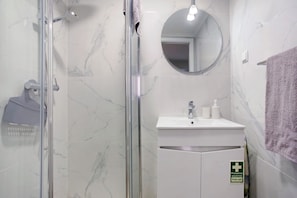 Une salle de bain avec une douche à parois de verre, un lavabo avec un miroir au-dessus et un panneau indiquant la présence de matériel de premiers secours sur le mur.