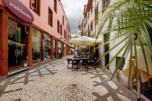 Une rue étroite avec un café, une boutique dont l’enseigne est visible, et un palmier.