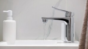 Un bagno moderno con un rubinetto cromato, un erogatore di sapone bianco e una parete in marmo.