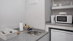 Una cucina con lavello, microonde ed elettrodomestico lavastoviglie, e un cesto bianco pieno di utensili.