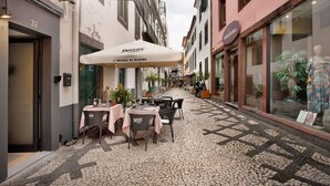 Una calle estrecha con mesas al aire libre, un café llamado 'Brisa' y una tienda con maniquíes.