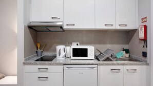 Cocina compacta con gabinetes blancos, microondas, lavavajillas y encimera de granito.