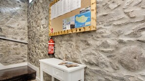 Una habitación con pared de piedra, un tablón de anuncios con varios avisos, un escritorio blanco con cajones y un extintor colgado en la pared.