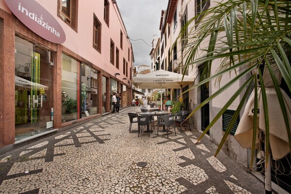 Une rue étroite, pavée de pierres, avec des tables en terrasse et un restaurant doté de parasols.