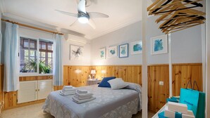 Un dormitorio con una cama, ventilador de techo, ventana con cortinas, paneles de madera y obras de arte en la pared.