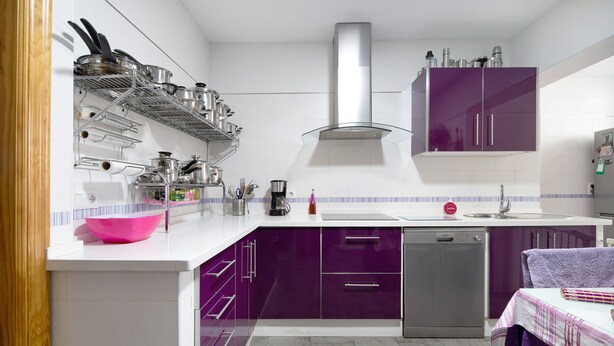 Una cocina con gabinetes blancos y morados, una campana extractora de acero inoxidable, un escurreplatos y una toalla morada en la encimera.