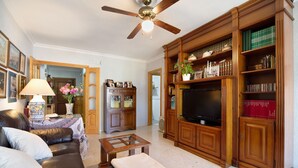 Una sala de estar con un sofá, una mesa de centro, un televisor y una estantería.