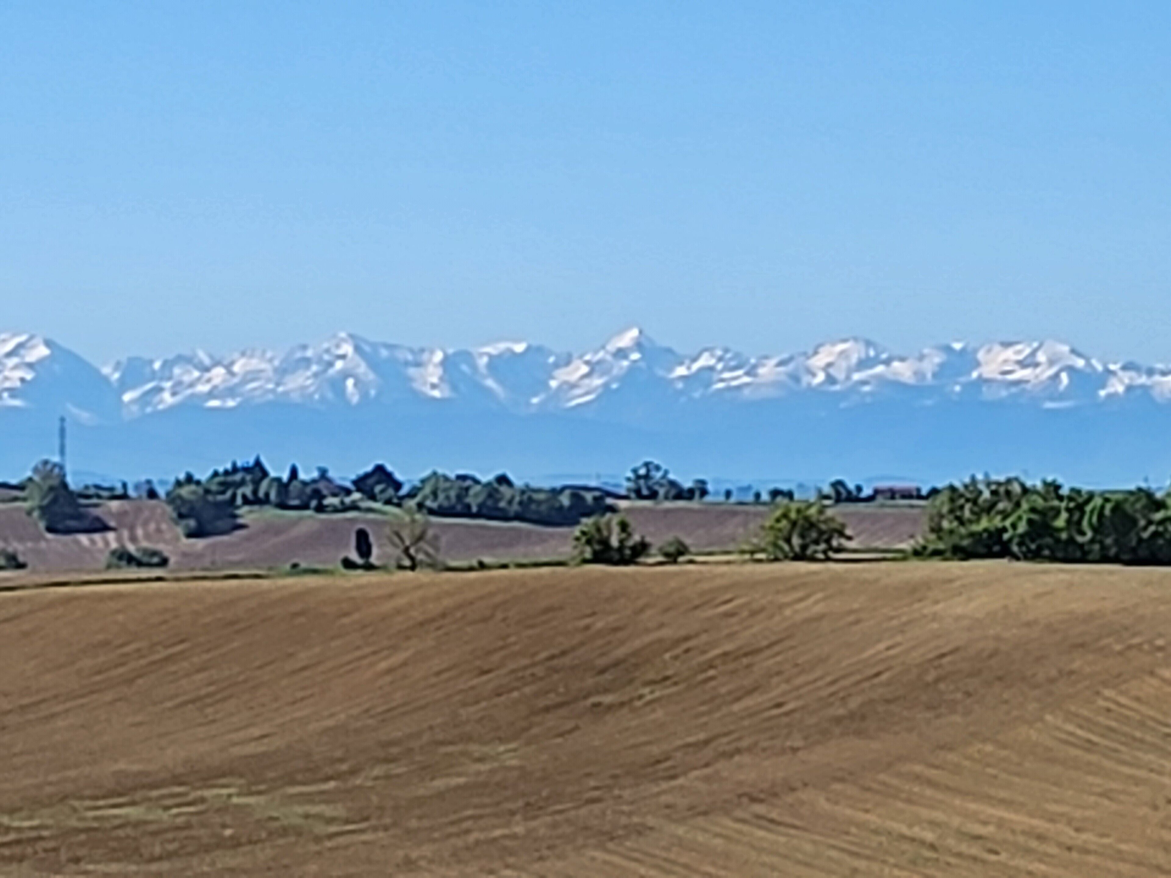 Un paisaje con un campo, árboles y una cadena montañosa al fondo.
