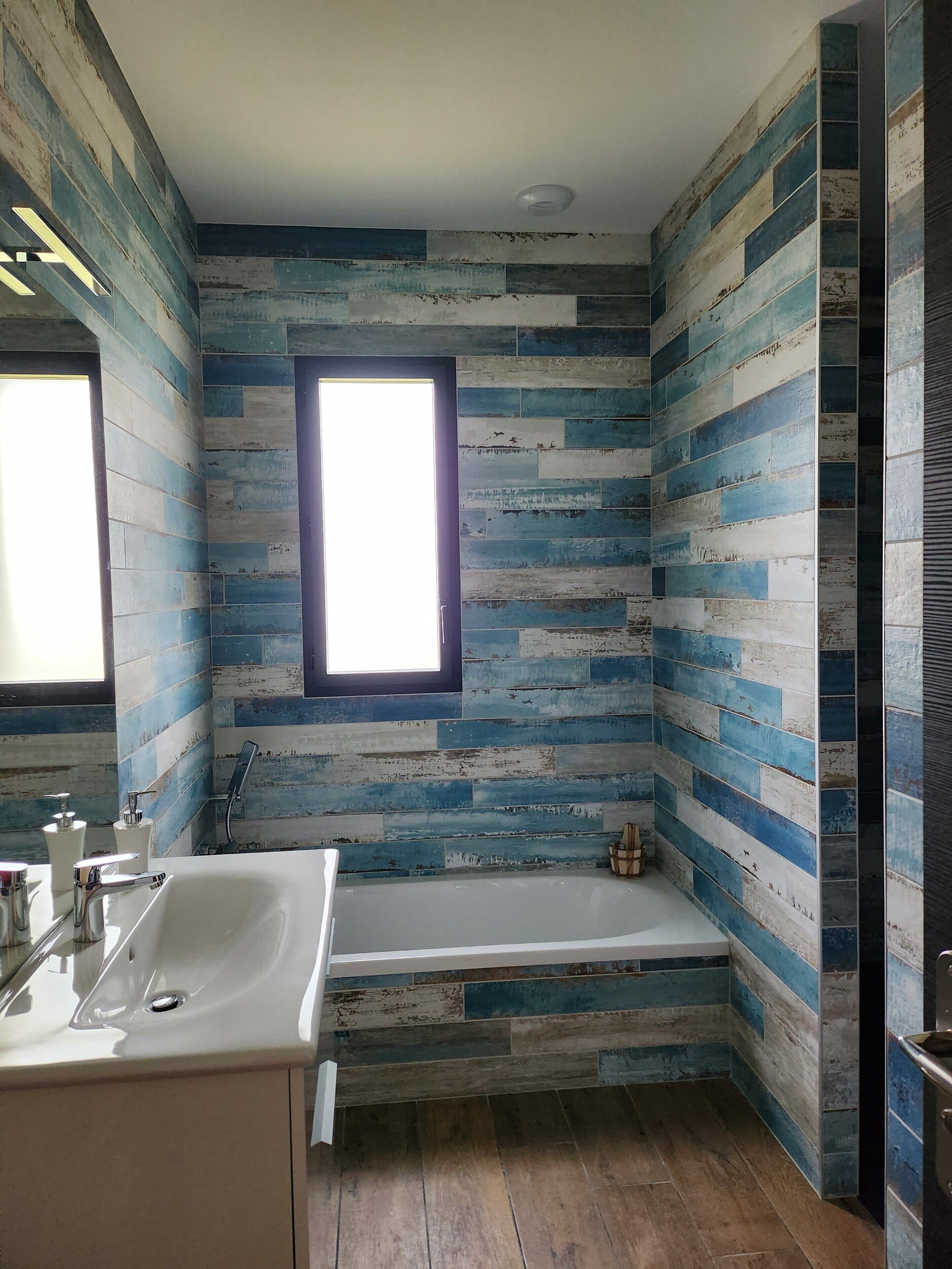 A bathroom with a wooden plank wall design, a window, a bathtub, and a sink with modern fixtures.