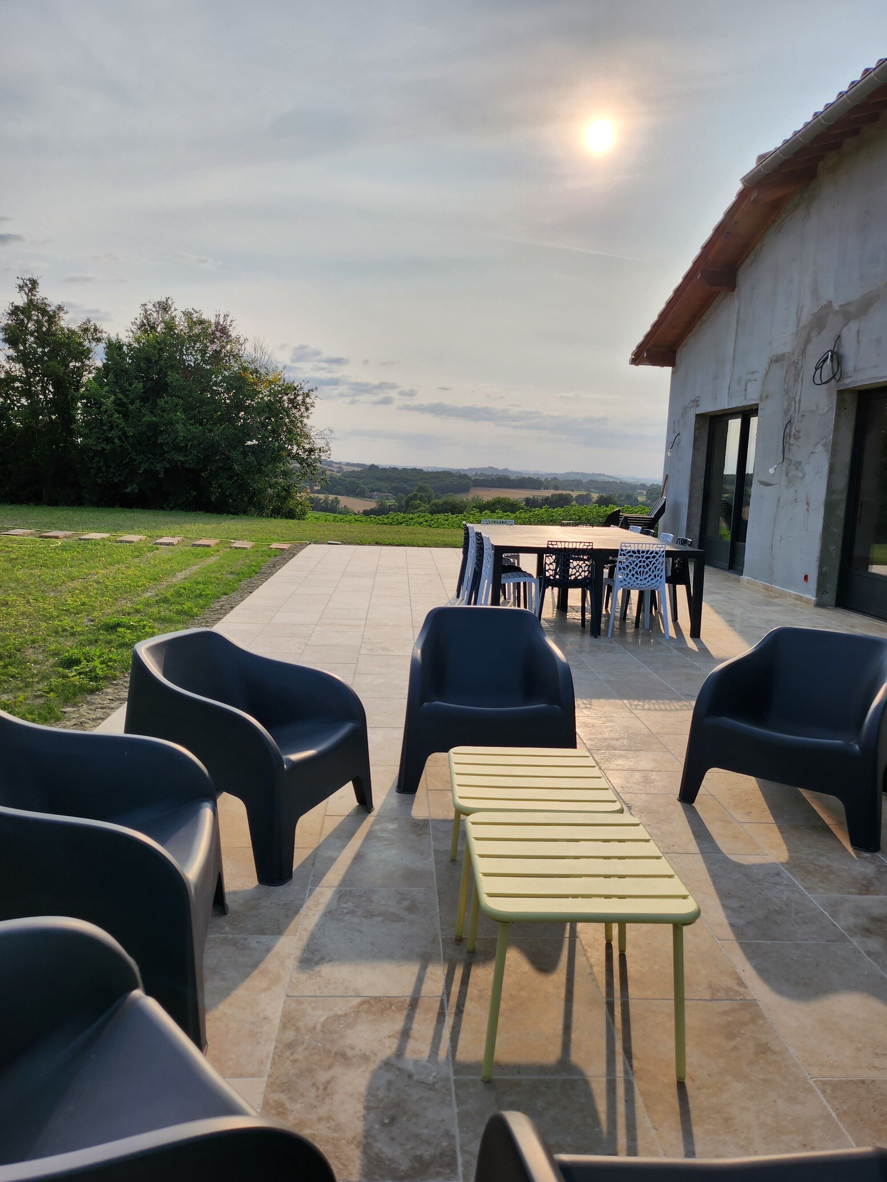 An outdoor patio with chairs and a table, a building with a tiled roof, and a view of the countryside.