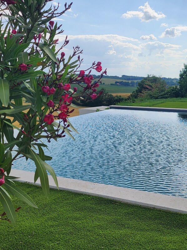A swimming pool surrounded by green grass and a tree with pink flowers.