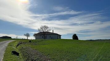 A rural house on a hill with a clear sky and a dirt path leading to it.