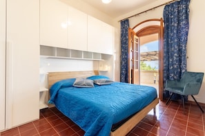 A bedroom with a bed, a chair, and a view through an open door.