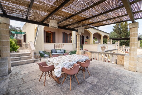 An outdoor patio with a table and chairs, a pergola, and a view of a building with arches.