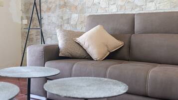 A brown leather sofa with a beige pillow against a stone wall, accompanied by two small round tables.