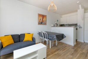 Un espace de vie moderne comprenant un canapé, une table à manger, des chaises, un coin cuisine et un luminaire suspendu.