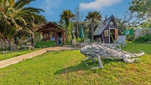A rustic wooden cabin with a thatched roof, surrounded by lush greenery and palm trees. - Chalet 'With Garden and Sea View 100m' with Sea View, Private Terrace and Garden (Plougastel-Daoulas)