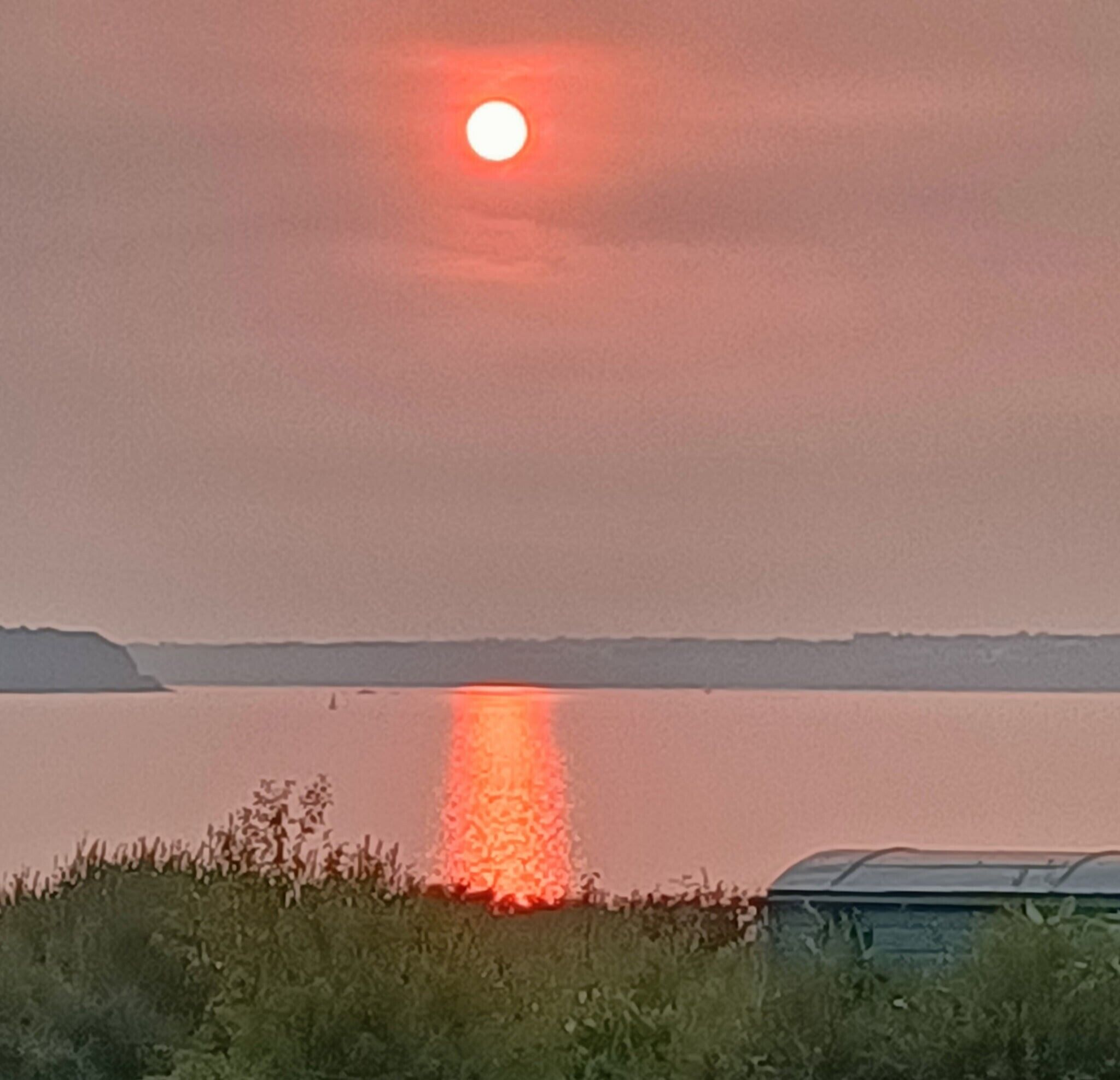 Ein Sonnenuntergang über einem Gewässer mit einer fernen Küste.