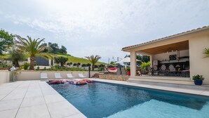 Una piscina con sillas de descanso, un porche cubierto y vistas a una colina.