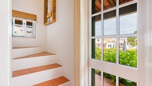 A staircase with terracotta steps, a window with a view of greenery and buildings, and a wooden-framed mirror on the wall.