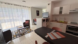 A modern kitchen with a dining area, a small TV, and a view through a large window.