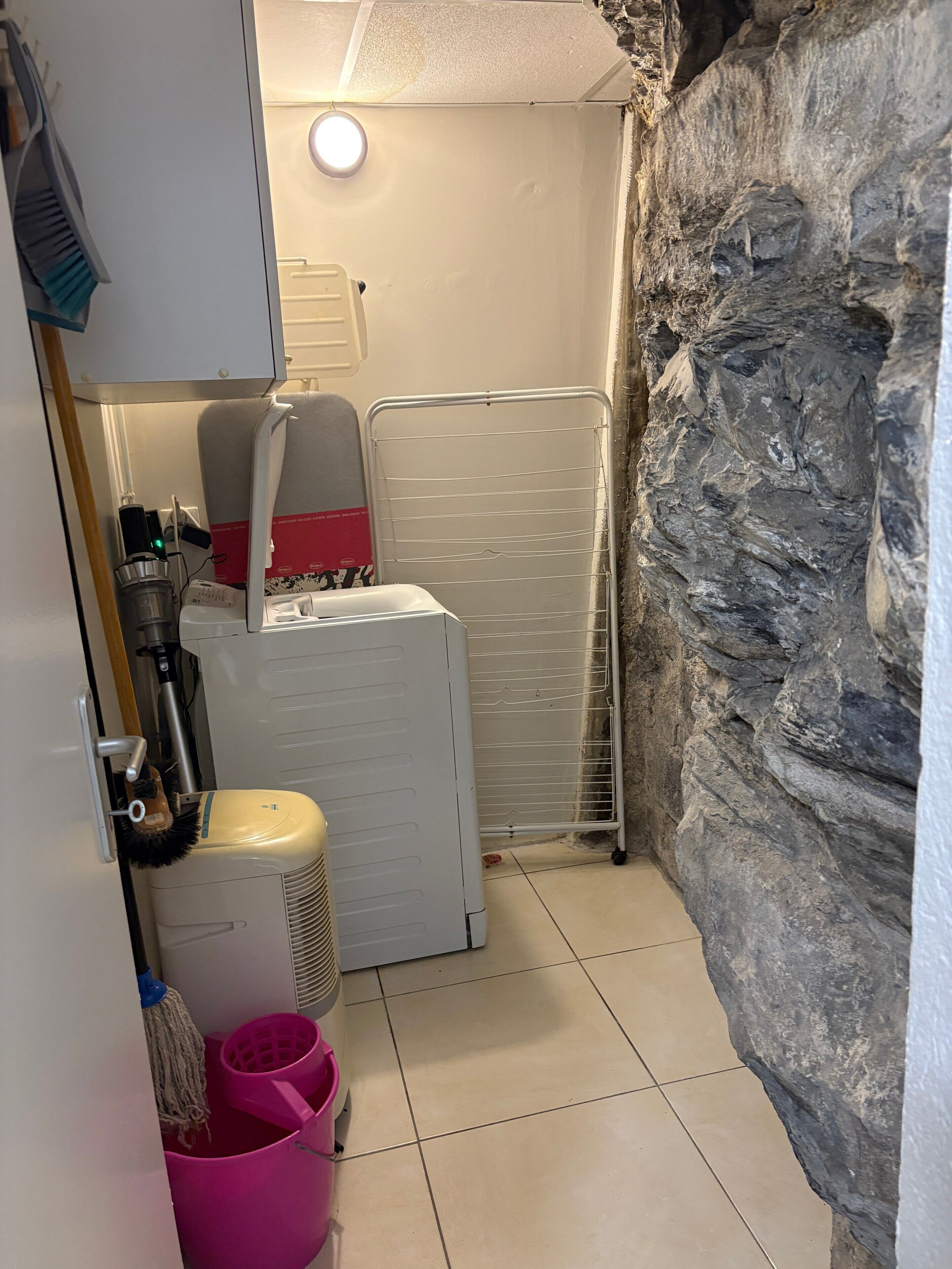 Un baño con pared de piedra, un calentador blanco, un tendedero y una fregona.