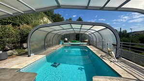 A covered swimming pool with a clear view of the sky, a slide, and a small inflatable ball.