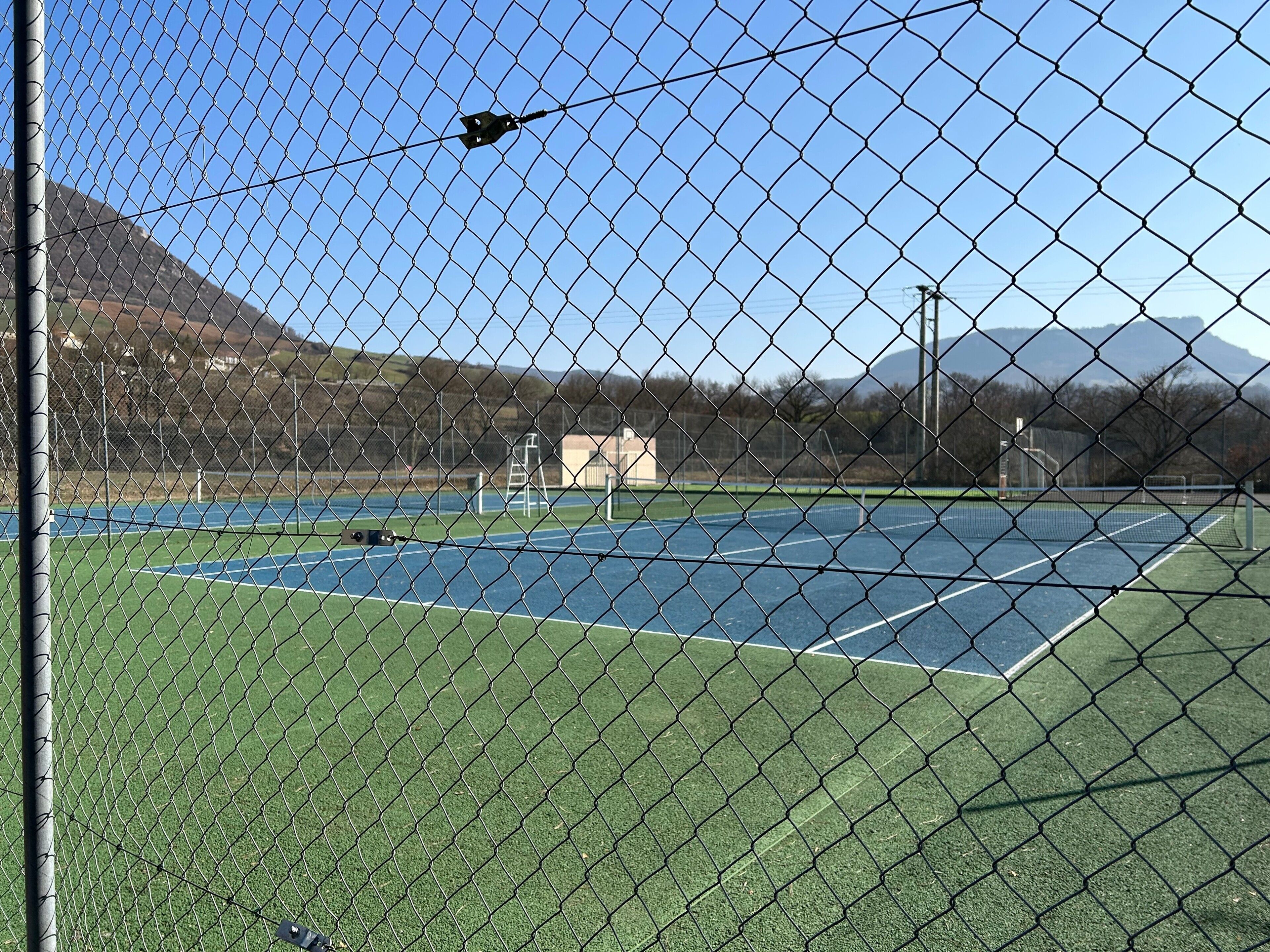 Un campo da tennis con una rete metallica, un palo di porta e un edificio sullo sfondo.