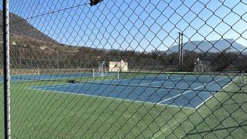 Un campo da tennis con una rete metallica, un palo di porta e un edificio sullo sfondo.