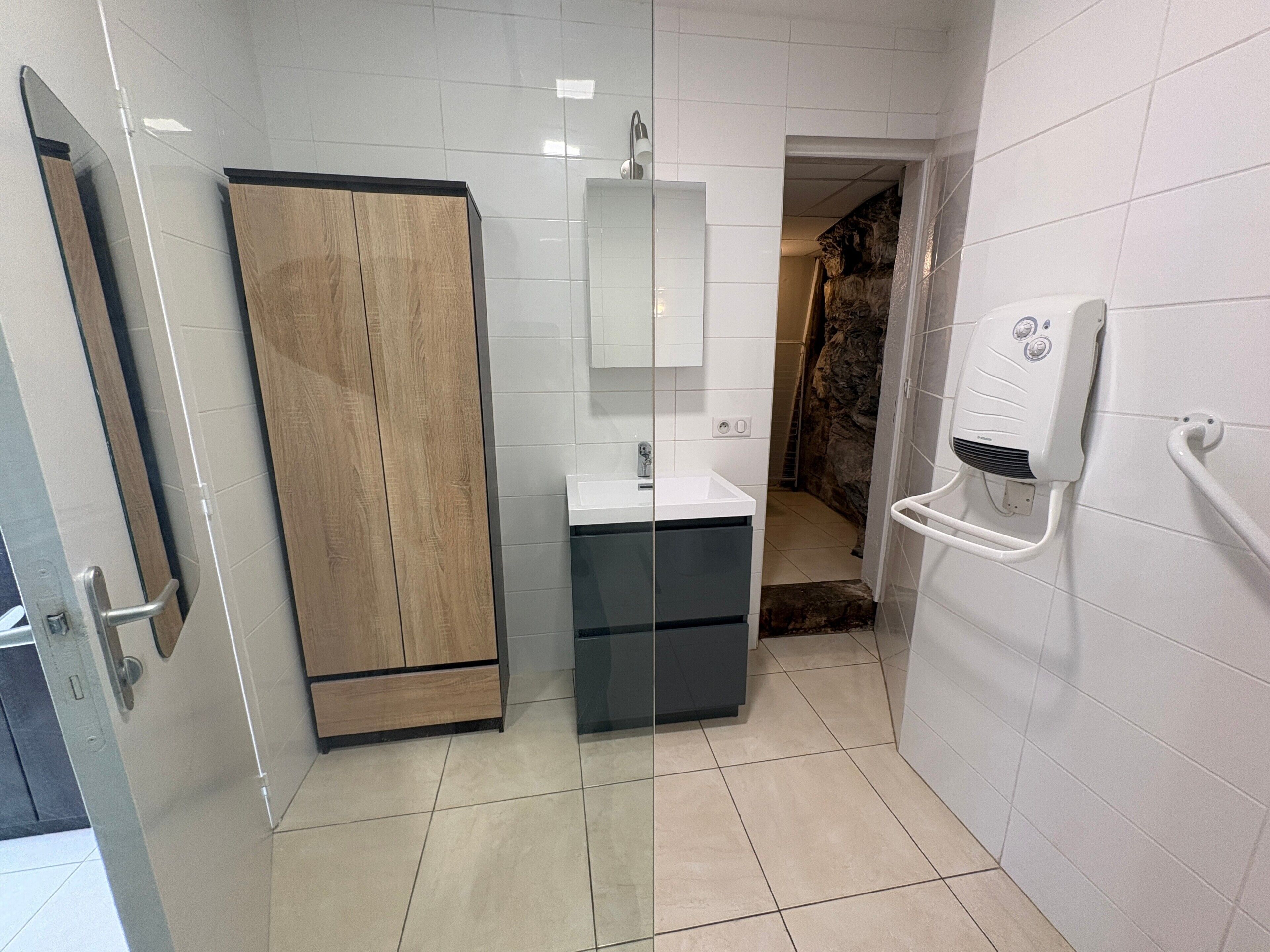 A bathroom with a wooden cabinet, a sink, a mirror, and a hand dryer.