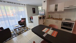 A modern kitchen with white cabinets, a microwave, and an oven. There is a dining area with a black table and chairs.
