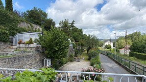A balcony with potted plants, a stone wall, and a view of a road with a fence.