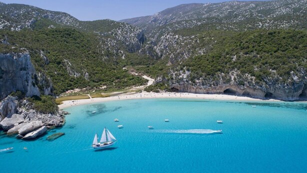 Una zona costera con un mar azul cristalino, acantilados rocosos y una playa.